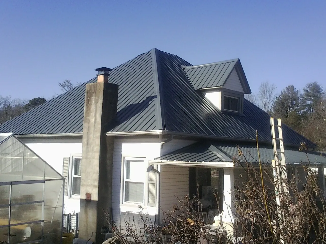Dark blue standing seam metal roof on a white farmhouse with dormer — Slate & Tile Roof Repair by Roofing Brothers in Saint Rose