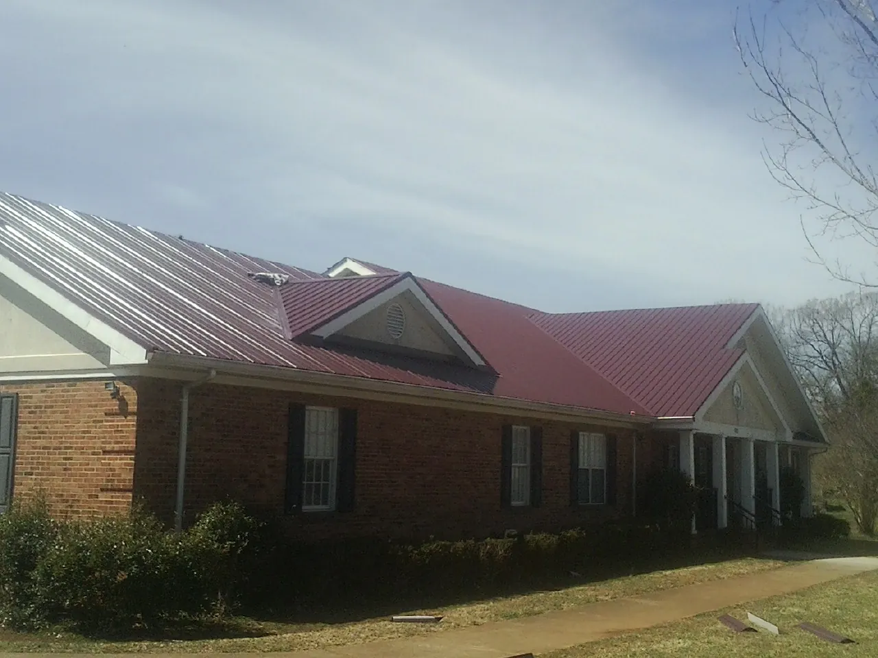Red metal roof with gabled entries on a long brick building, from a Hail Damage Roof Repair job in Saint Rose