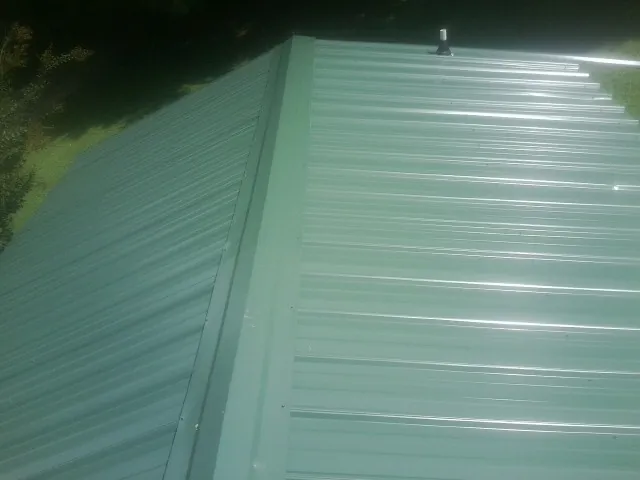New green metal panels meeting at the ridge of a roof — Flat Roof Repair work by our crew in Saint Rose