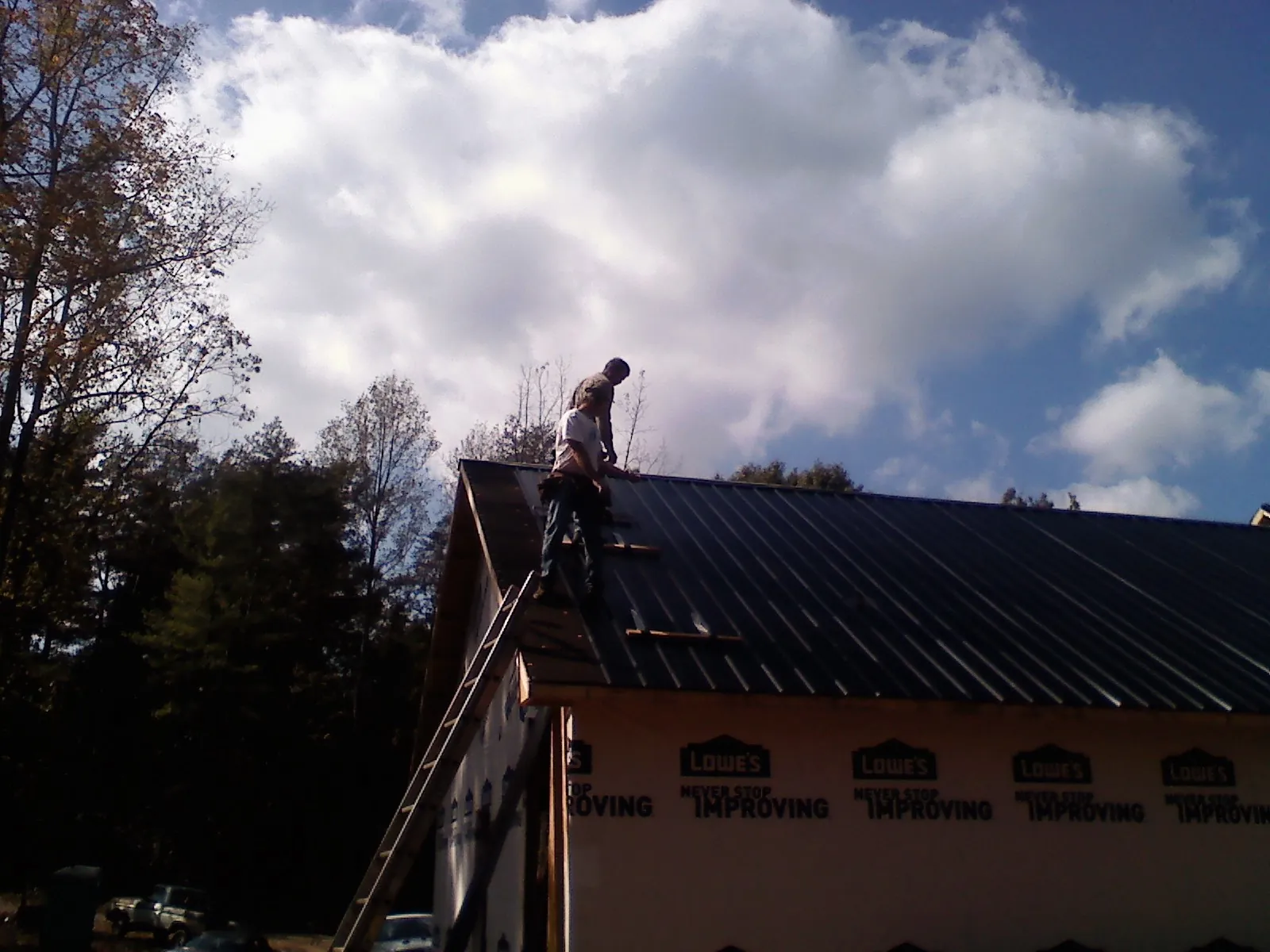 Roofer fastening dark metal panels high against a cloudy sky, from a Roof Inspection job in Saint Rose
