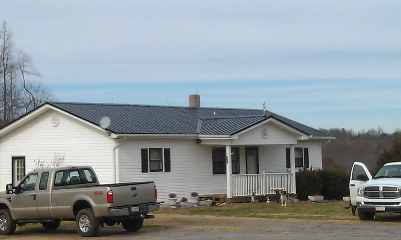 Finished dark metal roof on a white ranch home with work trucks parked in Saint Rose
