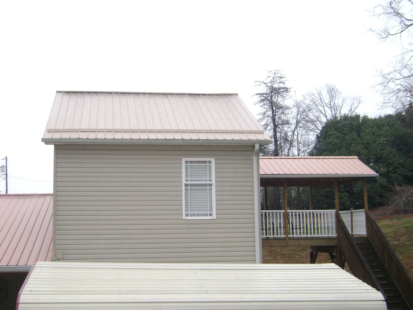 Tan metal roofs on a two story addition and attached porch, from a Roof Replacement job in Saint Rose